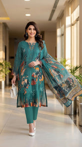 Full length front view of a smiling model walking through a bright hotel corridor carrying a white handbag, wearing a rich teal luxury lawn suit with abstract ikat floral placement print in orange, rust, and navy, V-notch neckline with embroidered orange and teal leaf motifs, multicolour ikat cuff border, plain teal cigarette trousers, and matching dark teal printed lawn dupatta with geometric chevron border draped over one arm