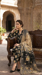 Model seated cross-legged on a Persian rug in a Mughal courtyard in a midnight black golden rose lawn suit with matching printed trouser and gold ombre dupatta
