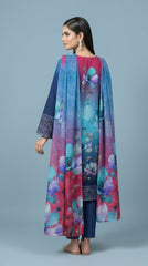 Full length front view of a model leaning against a green panelled wall in a teal-to-magenta ombré luxury lawn suit with scattered watercolour magnolia and anemone blooms, navy sleeves with blue paisley cuff border, plain navy cigarette trousers, and magenta-to-teal ombré chiffon dupatta draped over one arm