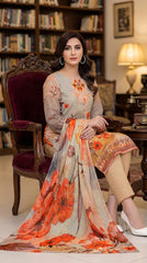 Model seated on a carved velvet armchair in a classic library setting wearing a warm beige luxury lawn suit with scattered orange-red lily and botanical floral print, embroidered orange and gold neckline placket, plain beige cigarette trousers, and cream-to-peach chiffon dupatta with oversized orange-red poppy and lily blooms pooling on the floor