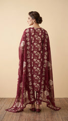 Back view of a model in a deep wine burgundy rose print luxury lawn suit with a cascading matching sheer organza dupatta featuring oversized ivory roses and structured woven border, warm beige studio background