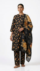 Model seated at a walnut desk in a modern study wearing a charcoal black Pakistani luxury lawn suit with all-over golden amber rose print and matching oversized rose chiffon dupatta draped over the chair