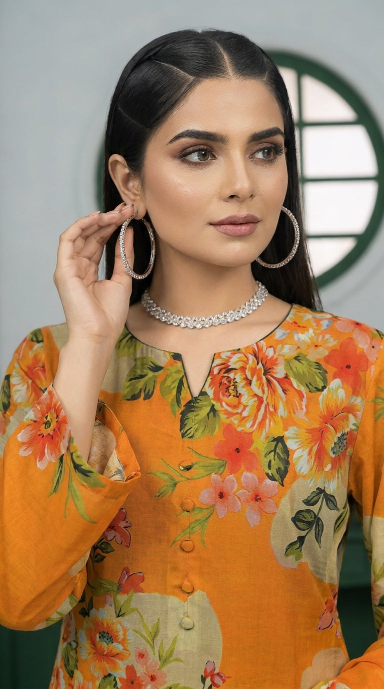 Full length front view of a model in a marigold orange luxury lawn suit with all-over oversized watercolour peony and hibiscus floral print, V-notch neckline with fabric button placket, plain orange cigarette trousers, and matching printed lawn dupatta with coral border, green-panelled studio background